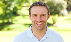 Smiling man outdoors in a white polo shirt.