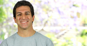 Smiling man in gray sweater with blurred natural background.