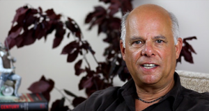 Portrait of a bald man smiling with a plant in the background.