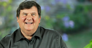 Smiling man in a dark shirt against a blurred green background.