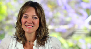 Smiling woman with shoulder-length hair against a blurred floral background.