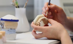 A person sculpting a dental mold with a brush tool.