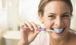 Woman brushing her teeth with a purple toothbrush.