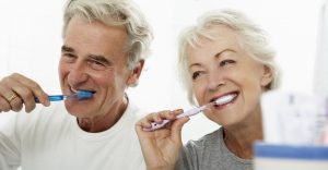 Elderly couple happily brushing their teeth together.