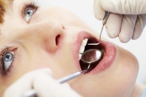 Dentist examining patient's teeth with dental tools.