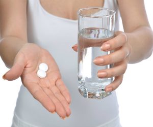 Person holding pills and a glass of water, preparing to take medication.