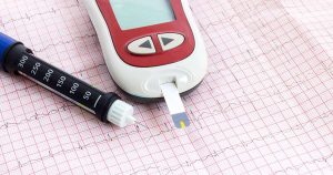 Blood glucose monitor with test strip and lancet on ECG paper.