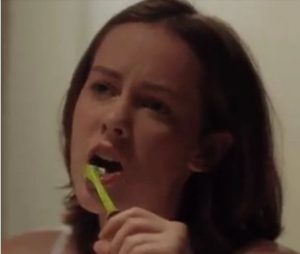 Woman brushing her teeth with a green toothbrush.