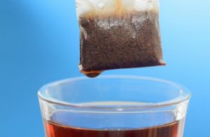 A tea bag dripping into a cup of tea against a blue background.