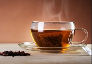 A steaming cup of tea with a tea bag inside on a clear saucer.