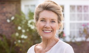Smiling elderly woman with light hair outdoors.