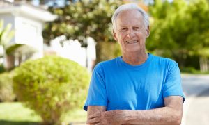 Smiling elderly man in a blue shirt outdoors.