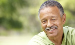 Smiling middle-aged man outdoors with a blurred green background.