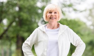 Smiling elderly woman outdoors with hands on hips.
